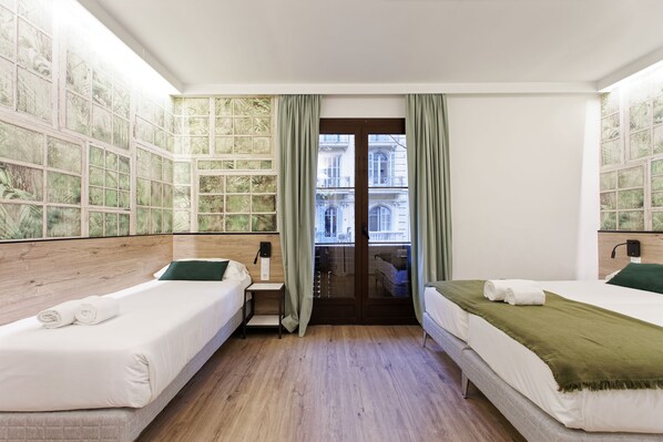 A hotel room with two beds, a wooden headboard, a small bedside table, a window with green curtains, and a view of a building through the window. - Casp Green House (Barcelona)