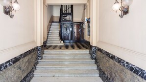 A marble staircase with a checkered floor pattern leading to a door labeled "PORTERIA." - Casp Green House (Barcelona)