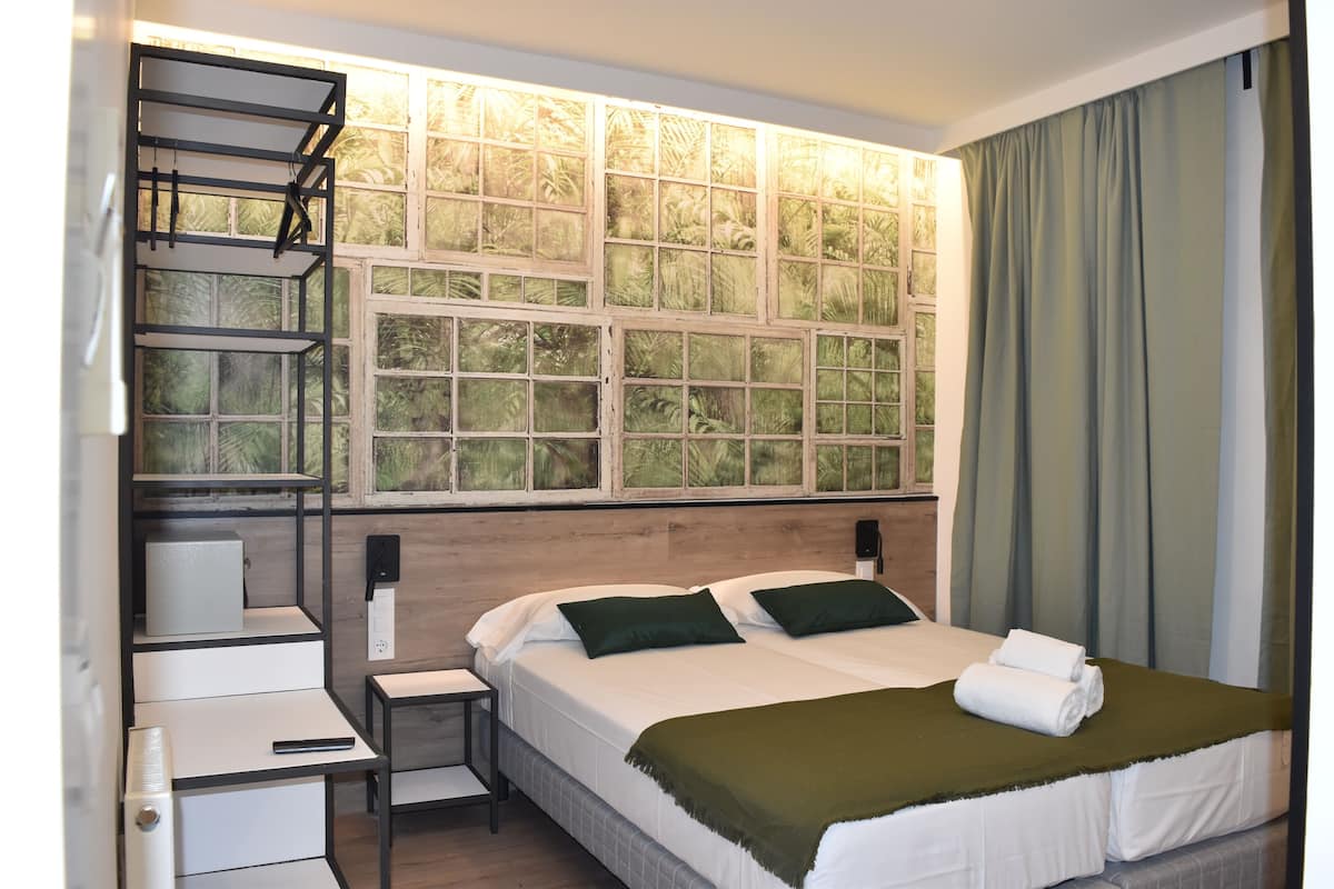 A hotel room with a bed, a desk, a chair, a window with a view of greenery, and a curtain.