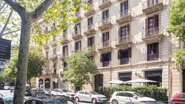 A multi-story building with balconies, parked cars, and a tree in the foreground. - Casp Green House (Barcelona)