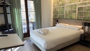 A hotel room with a bed, a desk, a window with curtains, and a wall with a green leafy pattern. - Casp Green House (Barcelona)