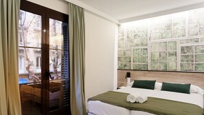A hotel room with a bed, a window with a view of buildings, and a door leading to a balcony. - Casp Green House (Barcelona)
