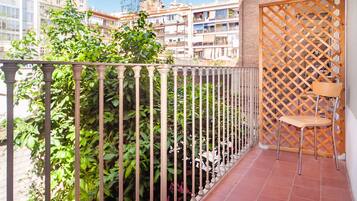 Een balkon met een metalen hekwerk, een houten lattenwand en een stoel.