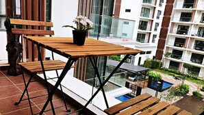 A balcony with wooden furniture, a potted plant, and a view of a swimming pool and residential buildings. - ETM Midhills Holiday Studio (Genting Highlands)