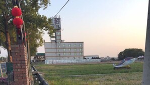 A building with a brick facade and a flat roof, surrounded by a grassy field and a body of water. - San Ho Business Hotel (Xiluo)