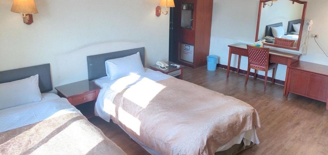 A hotel room with two single beds, a desk, a chair, a mirror, and a telephone.
