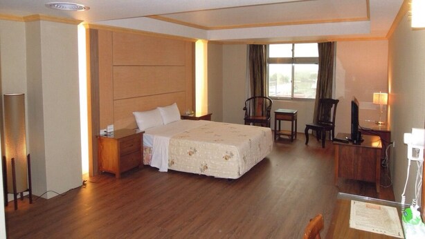 A hotel room with a large bed, a desk, a chair, and a window with curtains. - San Ho Business Hotel (Xiluo)