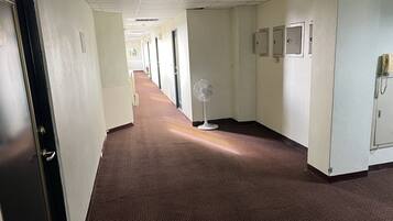 Un pasillo de hotel con suelo alfombrado, puertas y un ventilador.