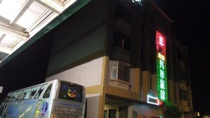 A building with a neon sign, a parked bus, and a tiled facade. - San Ho Business Hotel (Xiluo)
