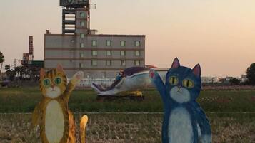 Two large cat sculptures in an open field with a building and a billboard in the background.