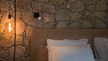 A room with a stone wall, a wooden headboard, and a bedside table with a book and a lamp.