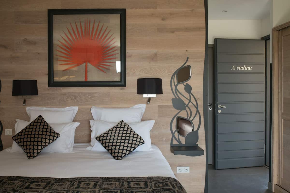 A neatly made bed with patterned pillows, a framed artwork above, and a door labeled "A vadina" to the right.