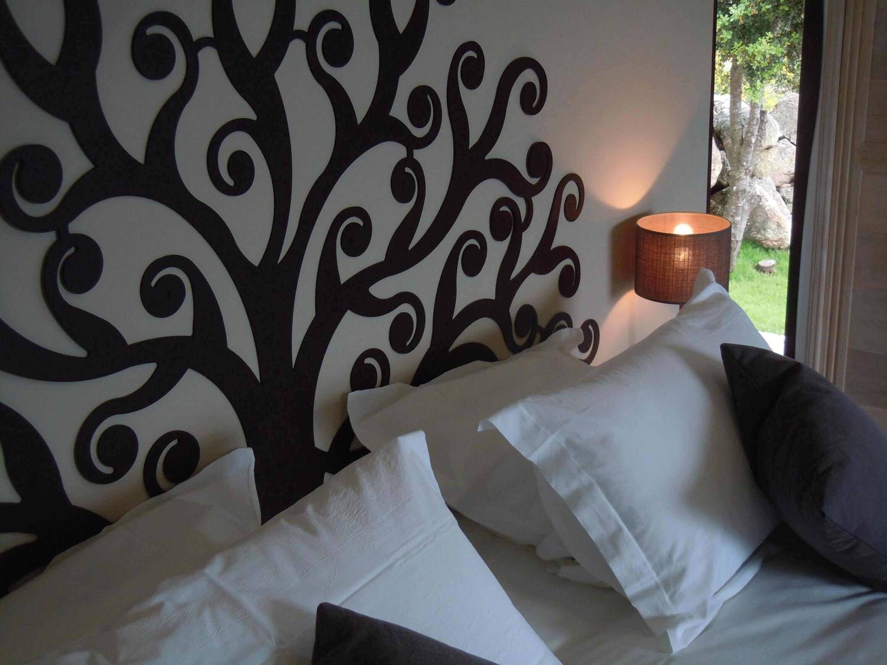 Un dormitorio con un panel decorativo en la pared, una cama con almohadas blancas y oscuras, y una lámpara de noche.