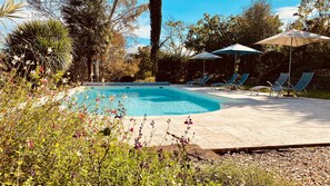 A swimming pool with lounge chairs and umbrellas, surrounded by greenery and flowers. - Secret Pyrénées (Lasseube)