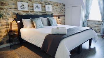 A bedroom with a stone wall, a bed with white bedding, two wall-mounted lamps, and a window with curtains.