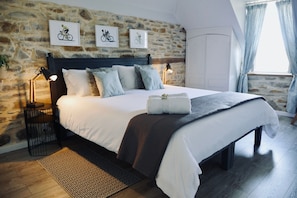 A bedroom with a stone wall, a bed with white bedding, two wall-mounted lamps, and a window with curtains. - Secret Pyrénées (Lasseube)
