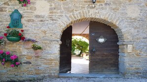 An arched stone doorway with a wooden door, a number plaque, and flower planters. - Secret Pyrénées (Lasseube)