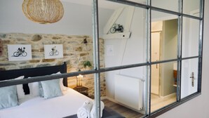 A bedroom with a stone wall, a bed with a headboard, a mirror, and a bicycle shelf. - Secret Pyrénées (Lasseube)
