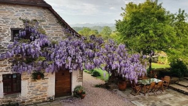 A stone building with a wooden door and window, surrounded by a gravel path and a table with chairs. - Secret Pyrénées (Lasseube)