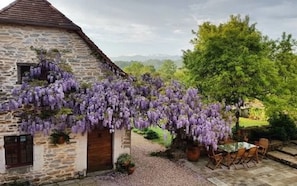 A stone building with a wooden door and window, surrounded by a gravel path and a table with chairs. - Secret Pyrénées (Lasseube)