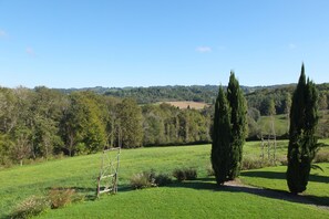 A rural landscape with a clear sky, green fields, and tall trees. - Secret Pyrénées (Lasseube)