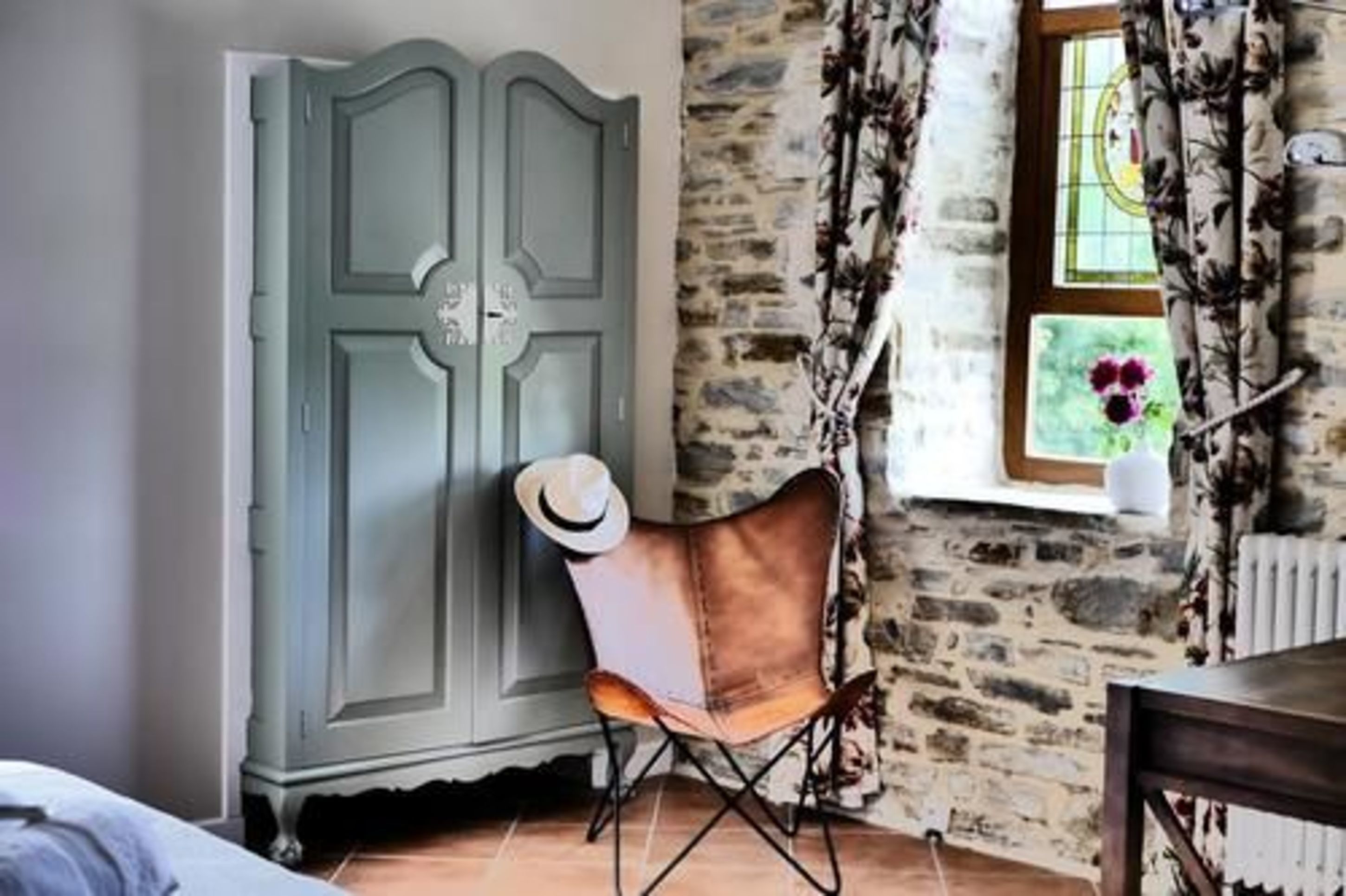 A room with a stone wall, a wooden cabinet, a leather chair, and a window with curtains.