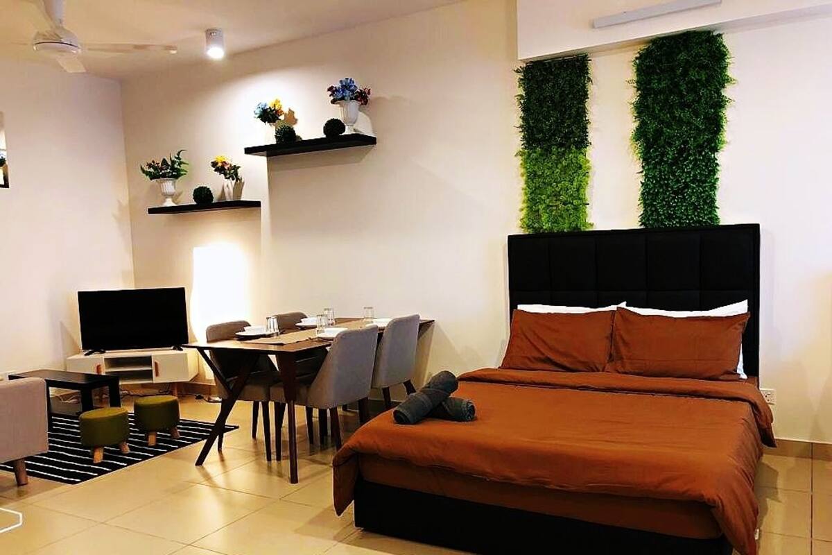 A modern bedroom with a bed, a desk, and a TV. There are plants on shelves and a green wall.
