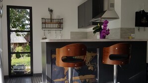 A modern kitchen with two bar stools, a map on the wall, and a window overlooking a garden. - La Griotte Chambre D'hotes (Honfleur)