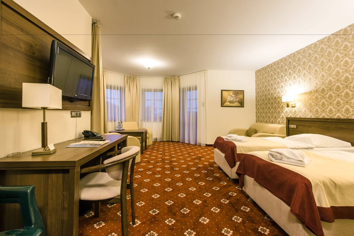 Habitación de hotel con escritorio, dos camas, televisor, teléfono y ventana con cortinas.