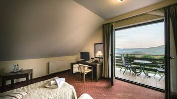 A hotel room with a bed, a desk, a chair, a TV, and a balcony with a view.