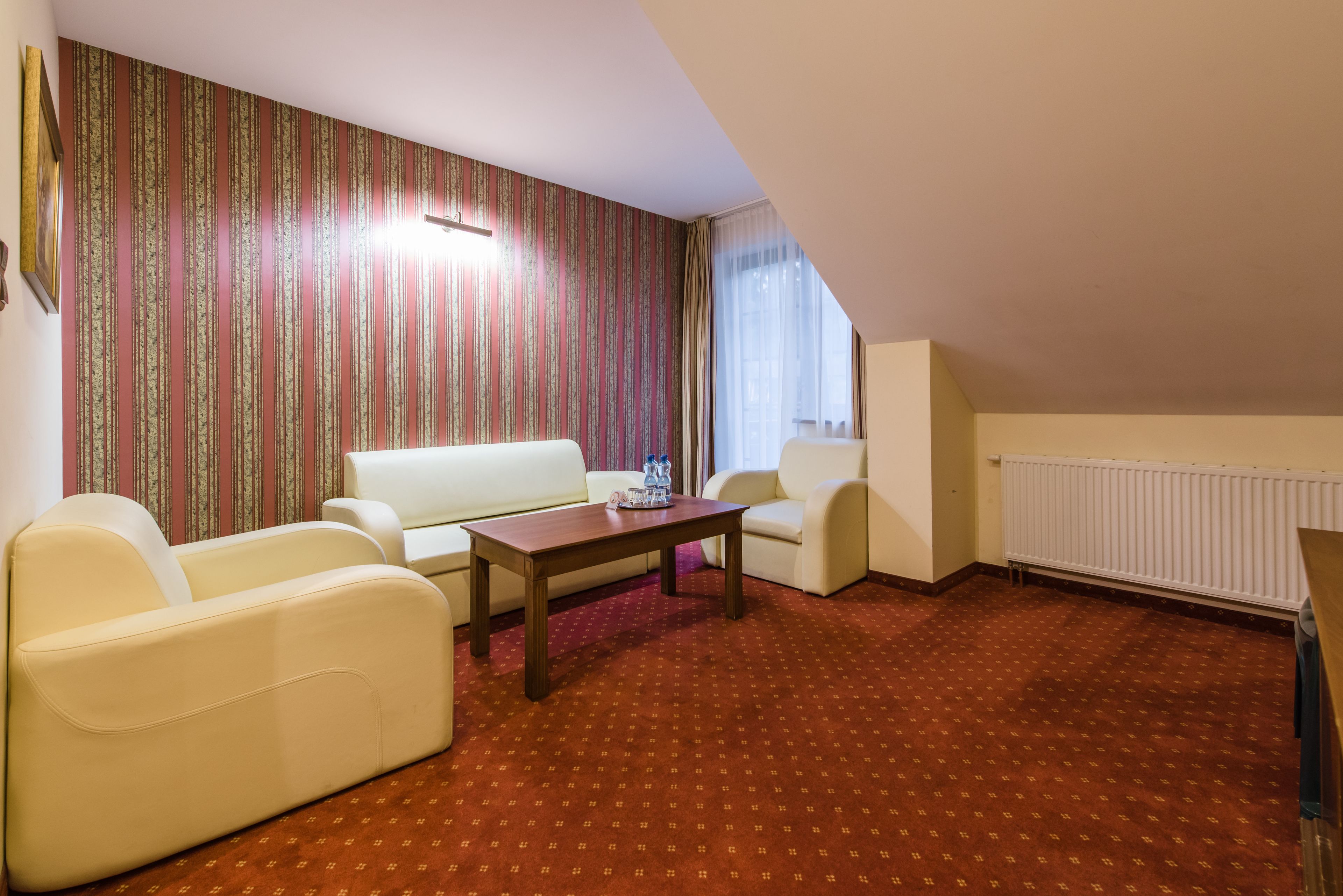 Un salón con alfombra roja, sofás blancos, una mesa de centro de madera y papel tapiz a rayas.