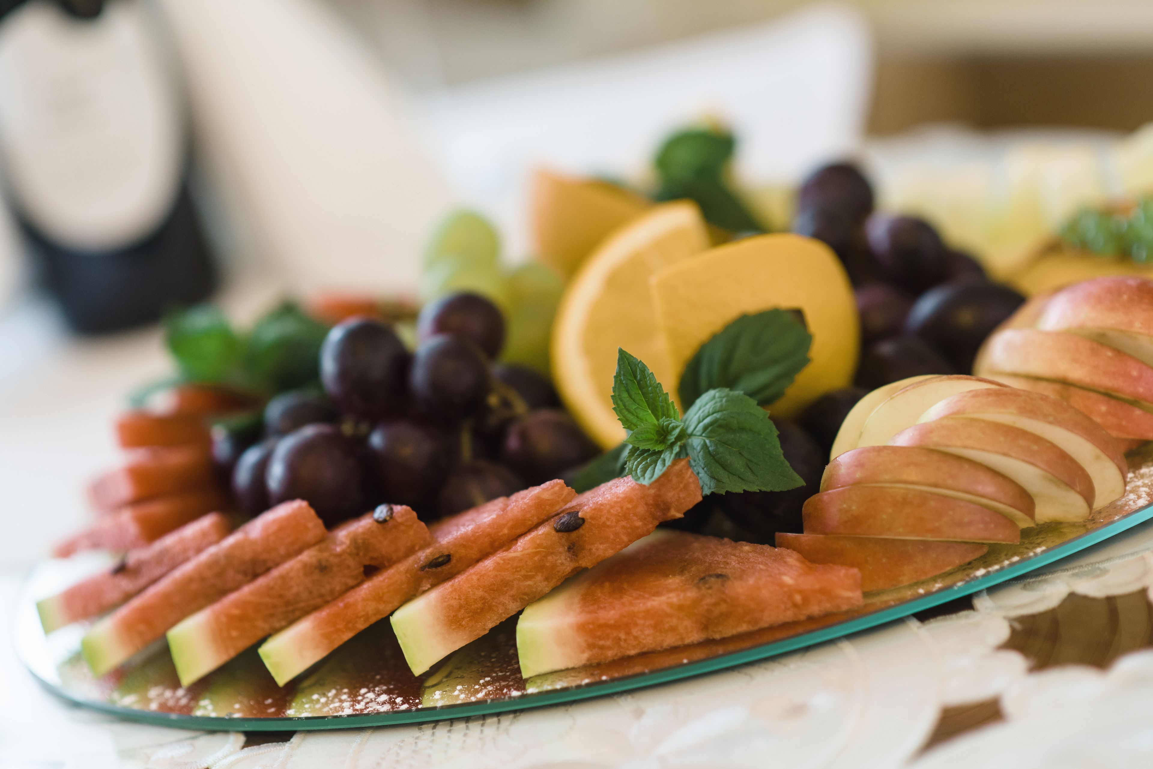 Una bandeja de frutas con uvas, manzanas y una loncha de queso sobre un plato de vidrio.