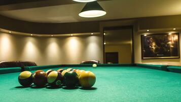Une table de billard avec les billes alignées, un luminaire au plafond et un tableau encadré accroché au mur.