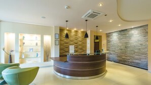 Una zona de recepción con un mostrador de madera curvada, estantes de vidrio e iluminación colgante moderna.
