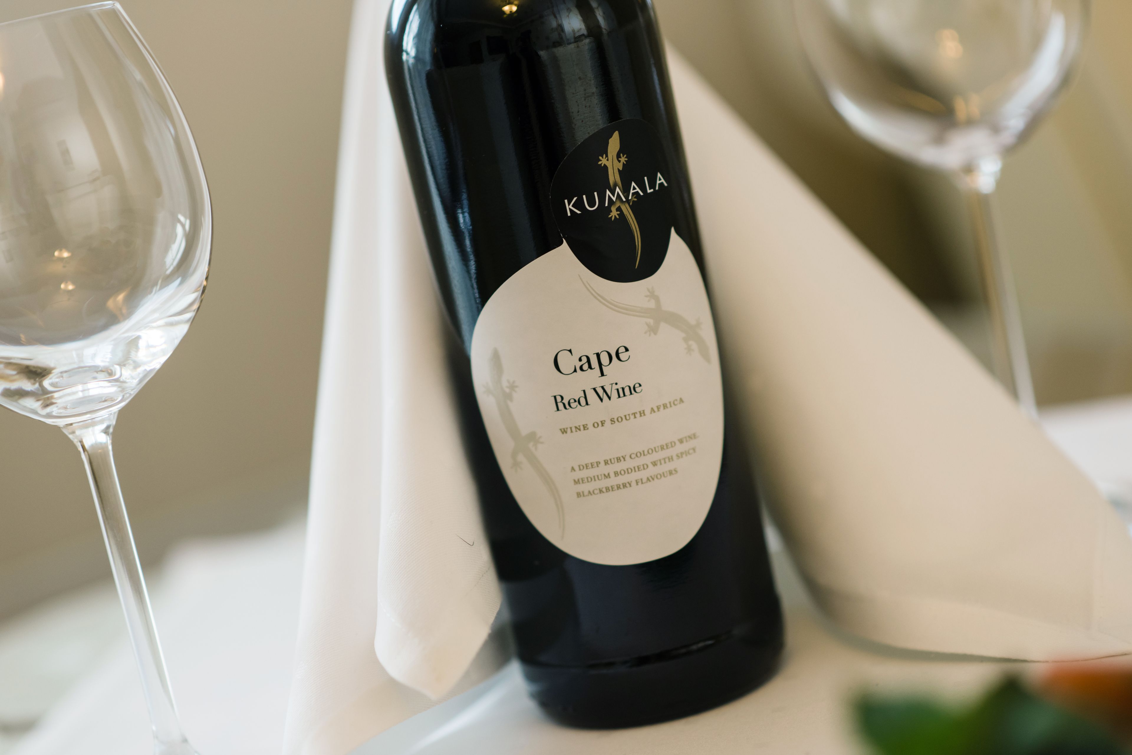 Une bouteille de vin rouge Kumala Cape, dont l’étiquette le décrit comme un vin d’une couleur rouge rubis intense, avec un corps moyen et des arômes d’épices et de mûres.