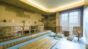 Una sauna con bancos y sillas de madera, suelo de baldosas y una ventana con persianas.