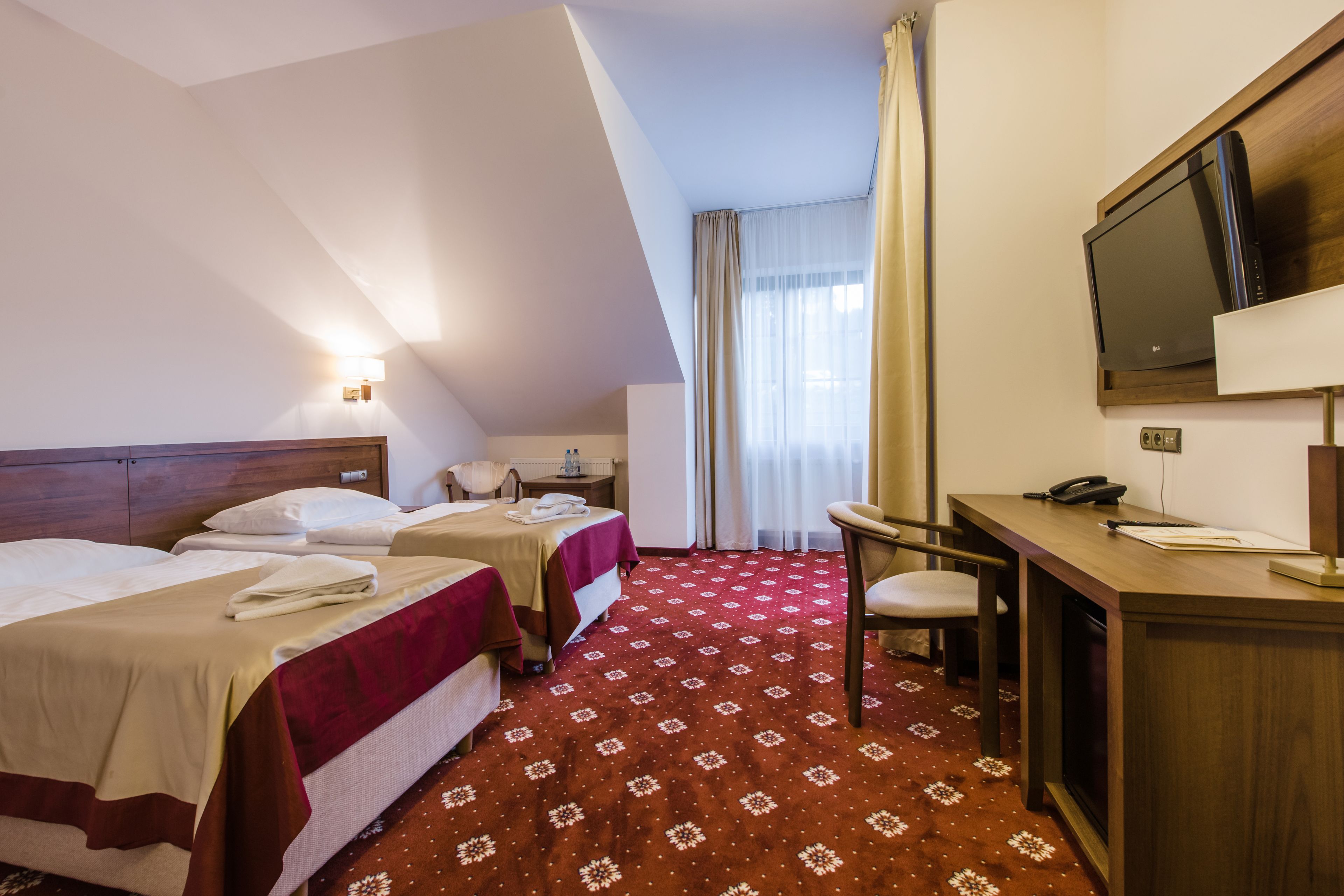 Une chambre d’hôtel avec deux lits, un bureau, une chaise, une télévision et une fenêtre avec des rideaux.
