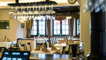 Un restaurante con mesas dispuestas para comer, un reloj en la pared y ventanas grandes con cortinas.