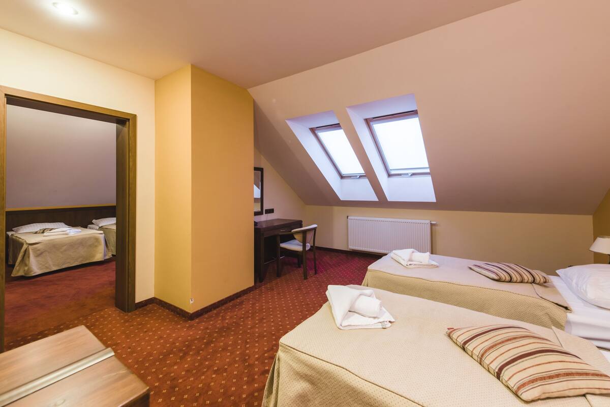 Habitación de hotel con dos camas, un escritorio, una silla y un tragaluz.