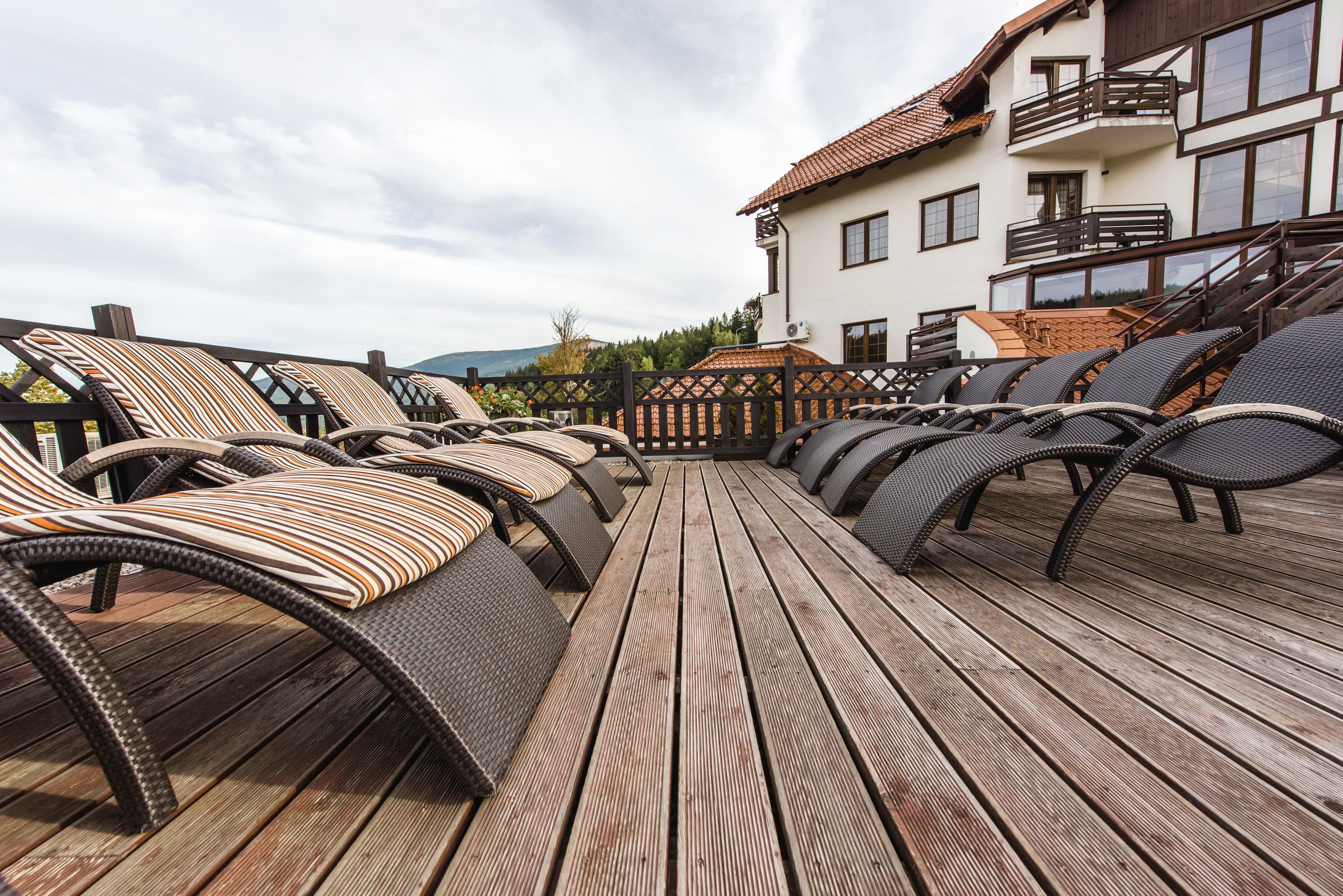 Une terrasse en bois avec des sièges extérieurs, un bâtiment blanc doté de balcons et un paysage montagneux en arrière-plan.