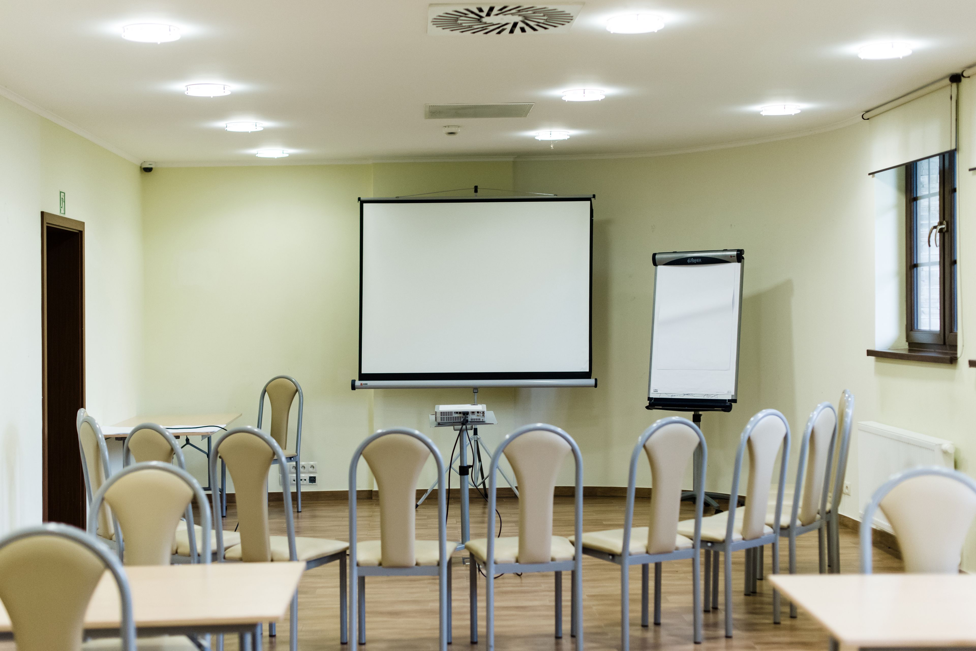 Un salón de conferencias con pantalla de proyector, una pizarra y varias sillas dispuestas alrededor de una mesa.