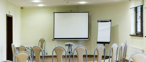 Un salón de conferencias con pantalla de proyector, una pizarra y varias sillas dispuestas alrededor de una mesa.