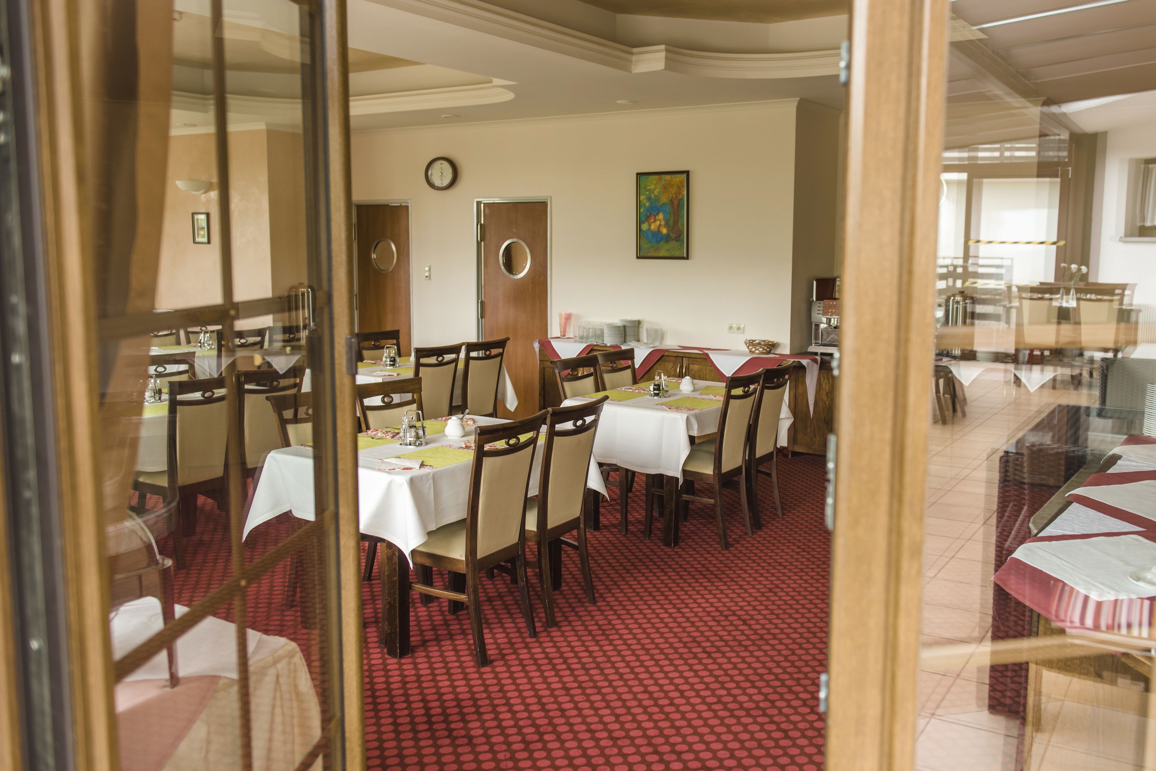 A dining area with multiple tables and chairs, a clock on the wall, and a painting.
