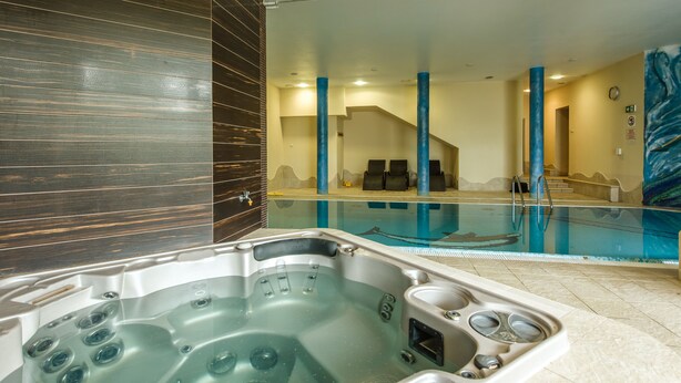 Una piscina interior moderna con hidromasaje, pilares azules y vistas al área de la piscina.