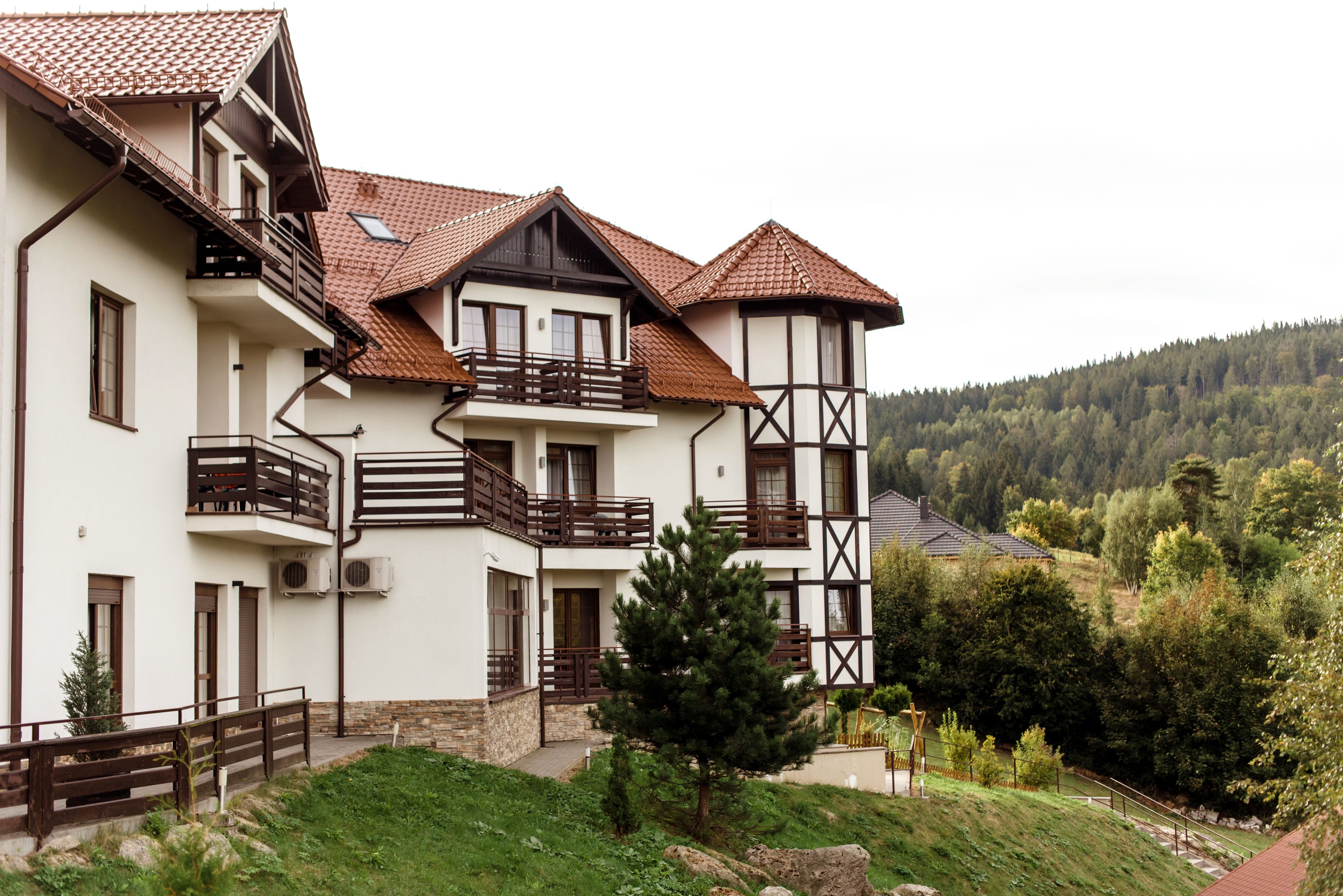 A multi-story building with balconies, a sloped roof, and a view of a forested hillside.