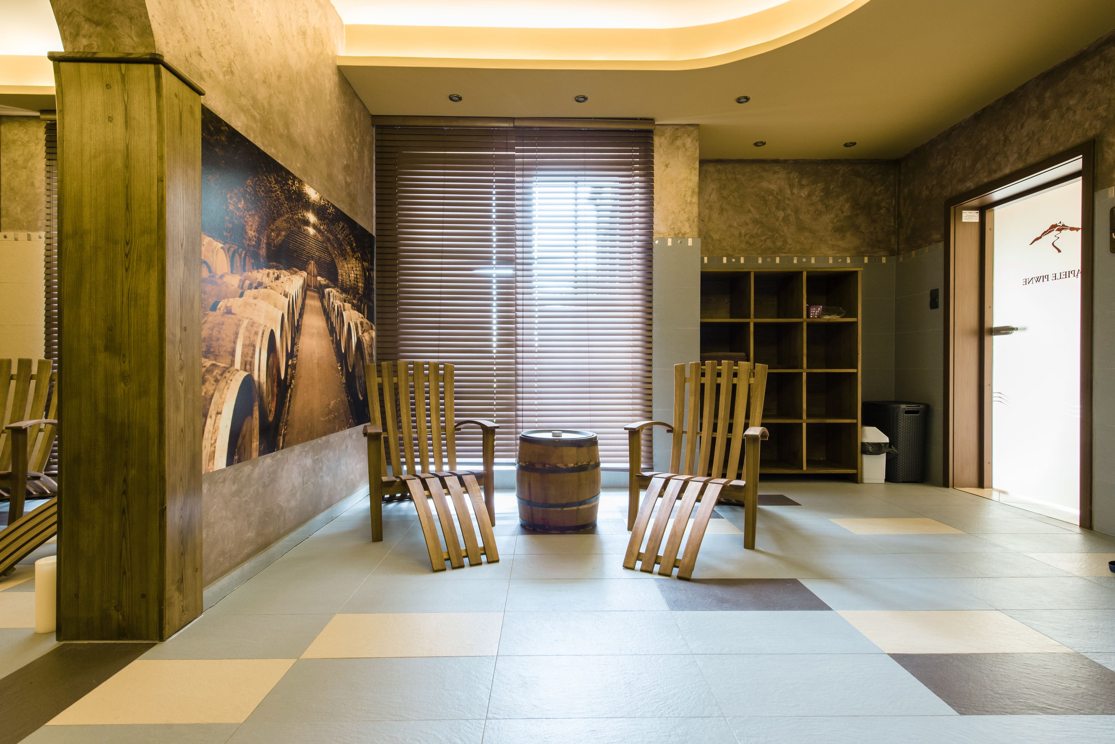 Un vestíbulo con piso a cuadros, sillas de madera, un barril, una estantería y un mural.
