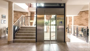 Un interior moderno con una escalera que lleva a un ascensor, suelo de baldosas y pared de ladrillo.