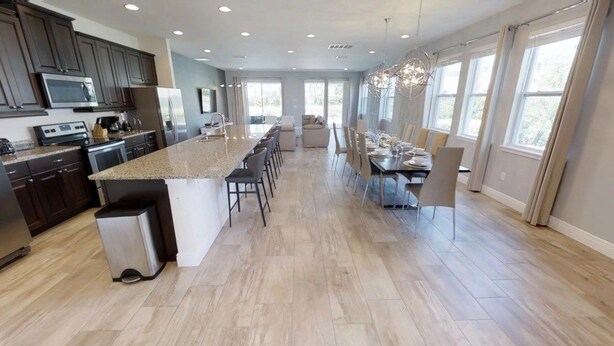 A spacious kitchen with a large island, dark wood cabinets, stainless steel appliances, and a dining area with a chandelier.
