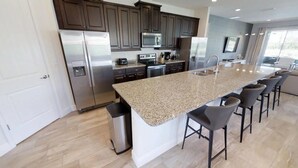 A modern kitchen with dark cabinets, stainless steel appliances, a granite countertop, and bar stools.