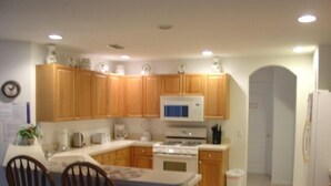 A kitchen with wooden cabinets, a microwave, a stove, and two wooden chairs. - Ahr137 - Tuscan Hills - 4 Bed 3 Baths Villa (Davenport)